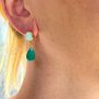 A woman with blonde hair wearing a drop earring with green stones.